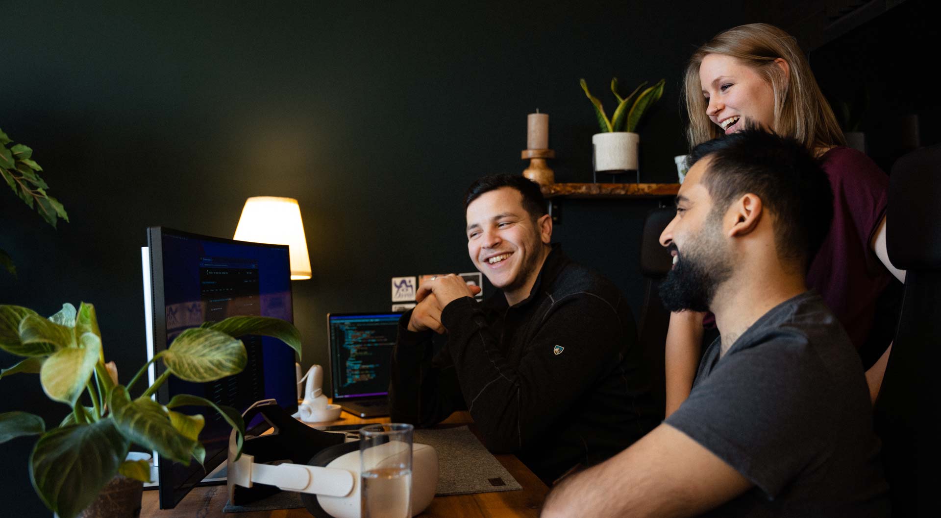Three people standing in front of a computer and talking about work.