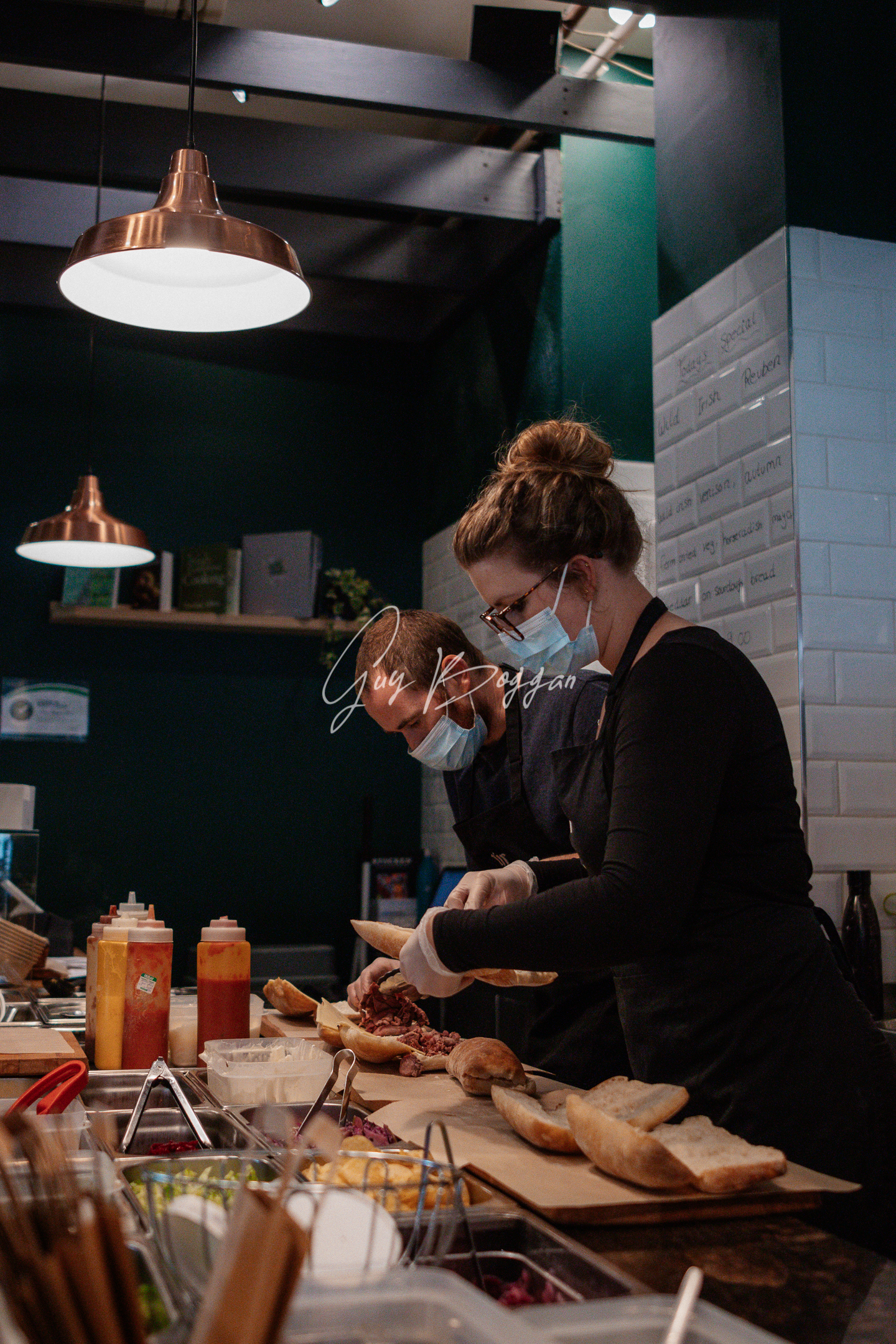 Two people wearing masks making sandwiches behind a deli counter