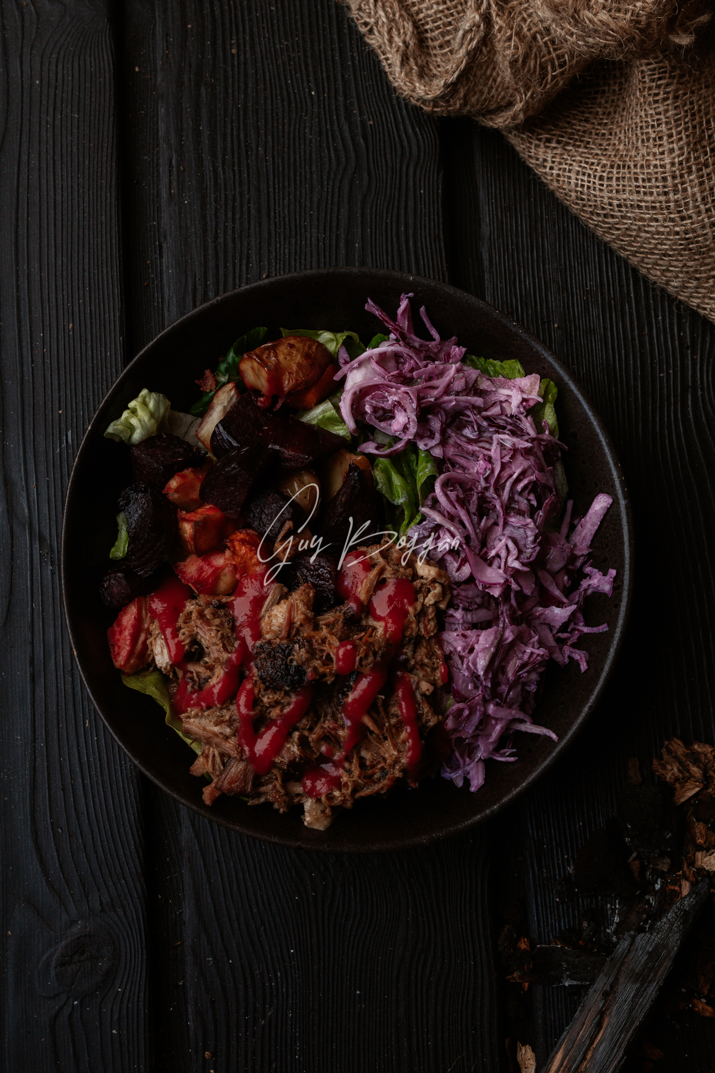 A top down shot of colourful salad in a black bowl sitting on a dark wood surface