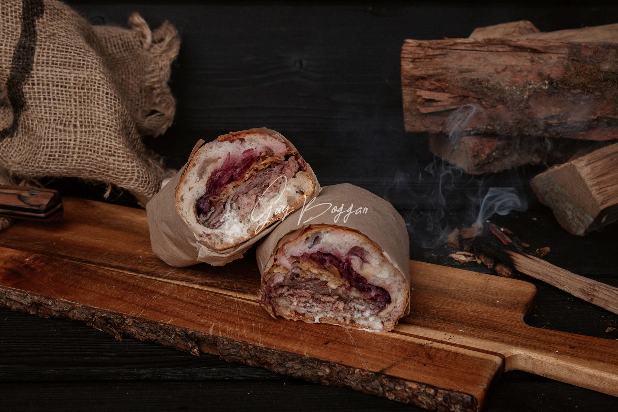 A sandwich cut in half sitting on a wooden board with a smoking ember beside it