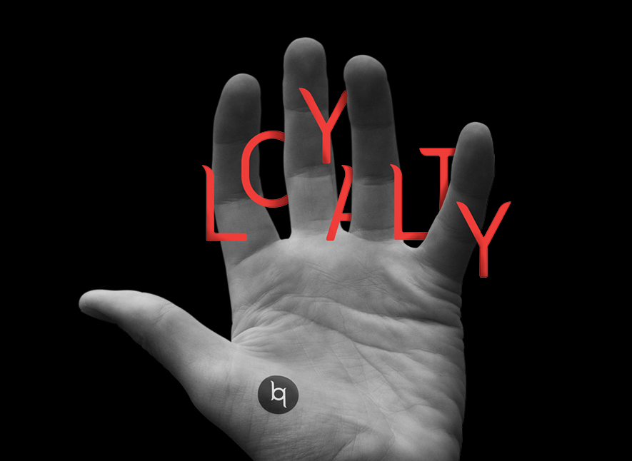 A dramatic black and white photo of a white male's hand with the words the word loyalty in a dramatic font floating between the fingers and a logo tattoo. 