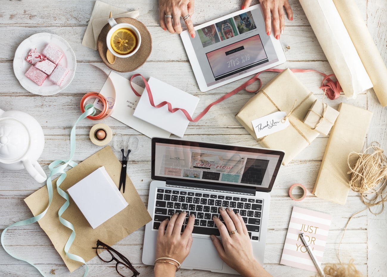 Two people with a laptop and a tablet shopping online on a table with gift wrapping paper