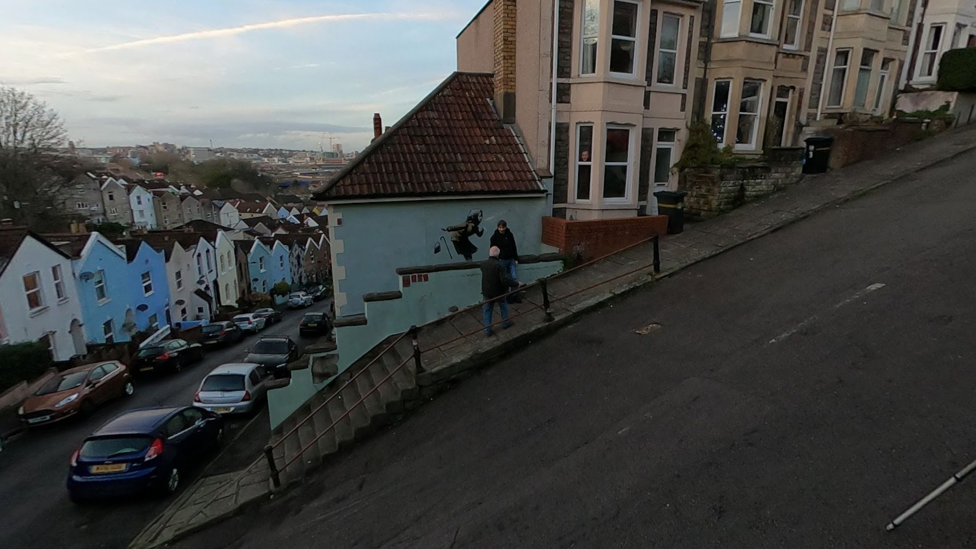 Banksy graffiti of an elderly lady sneezing very hard, on a building wall in Bristol, England in December 2020, captured by Google Street View.