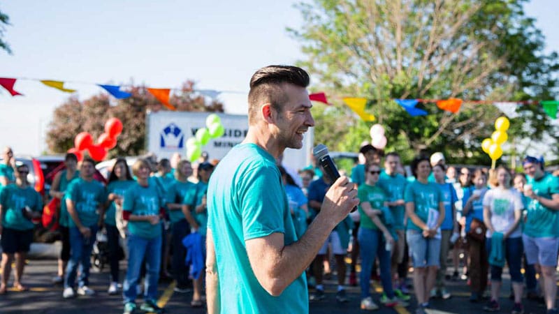 Man outdoors holding a microphone talking to people around him