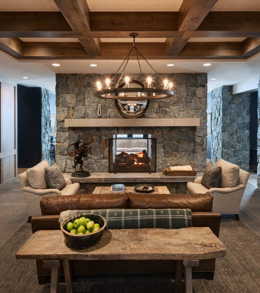 Luxury ski lodge with a brown leather couch, beige chairs, stone fireplace and chandelier.