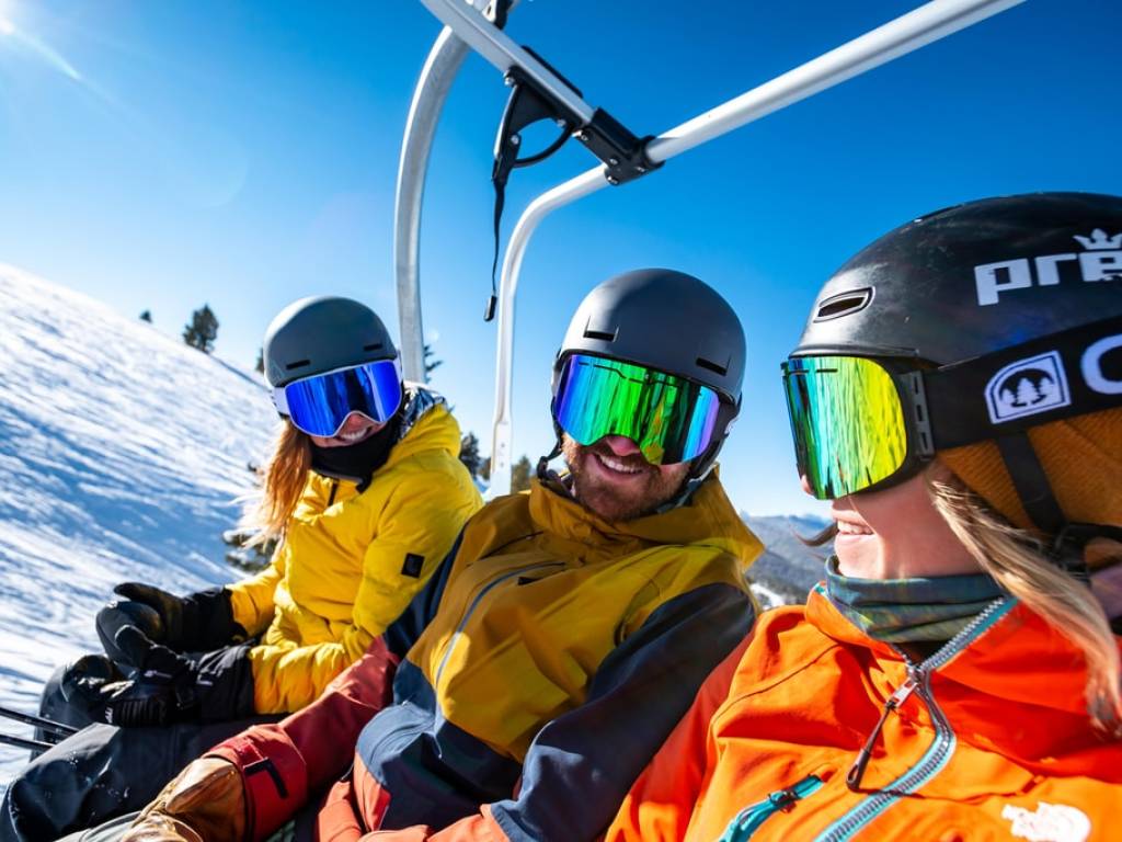 Three people dressed in ski gear riding on a ski lift.