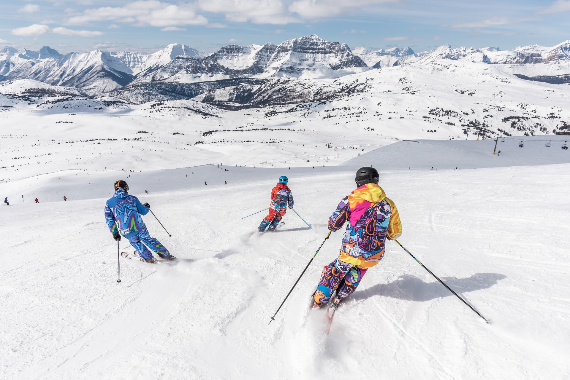 Three people dressed in ski gear skiing down a snow covered mountain.