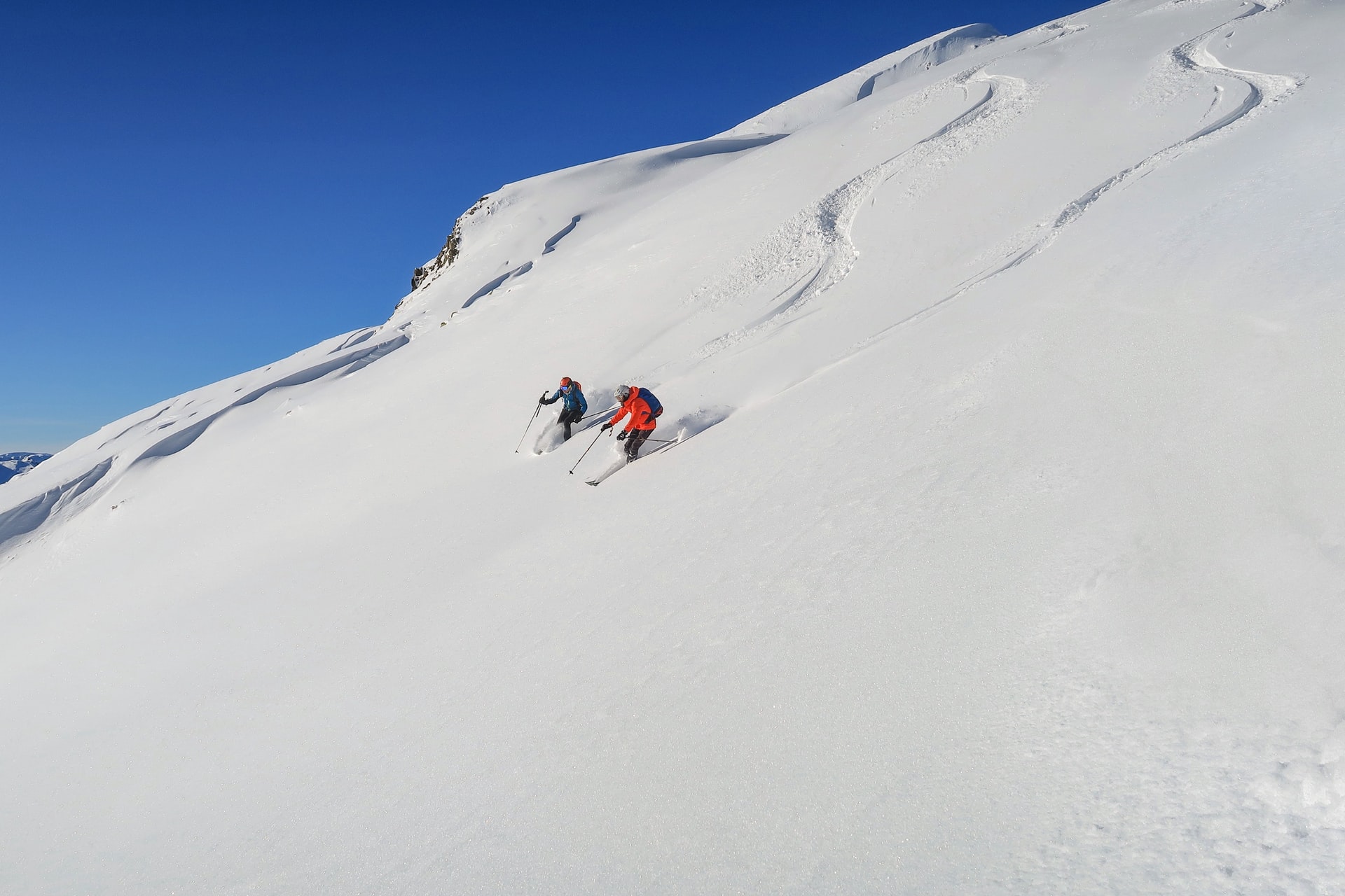 Two people dressed in ski gear skiing down a snow covered mountain.