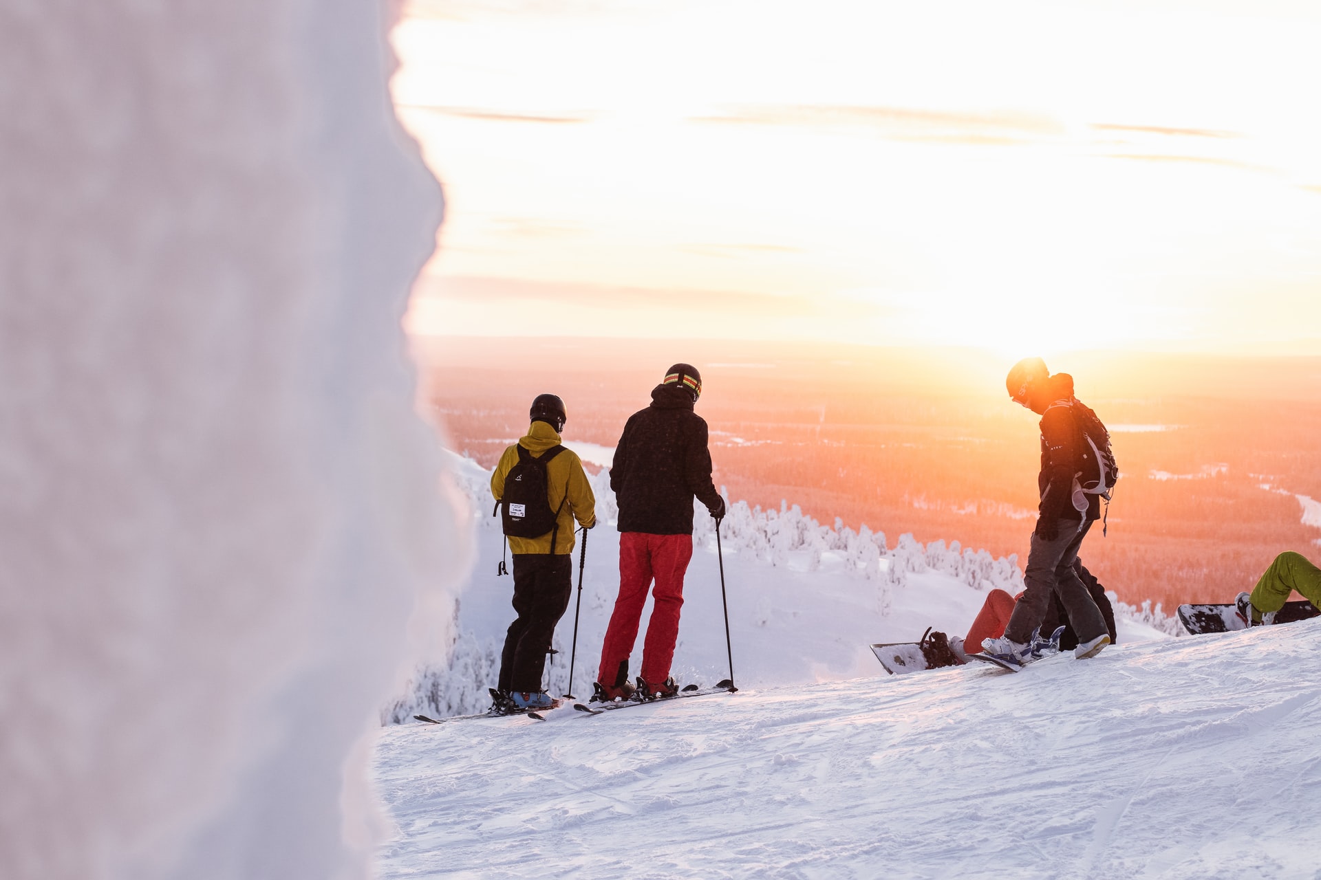 Three people dressed in ski gear standing on a mountain top looking at the horizon during sunset.
