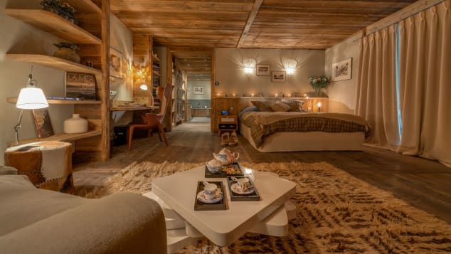 A luxury ski lodge resembling wood cabin. There is a beige chair with side table, a large bed and lights everywhere.