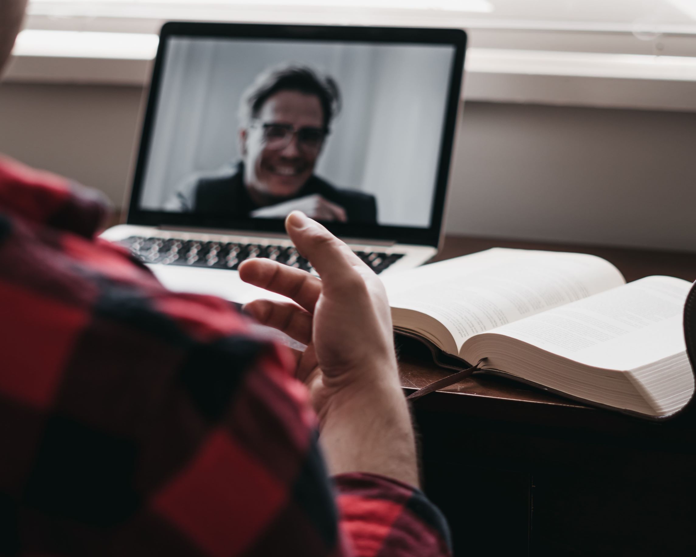 Mann sitzt vor Laptop und offenem Buch