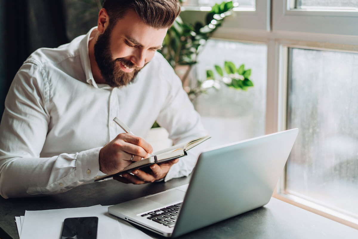 Work from home schedule: man happily noting things down in his notebook