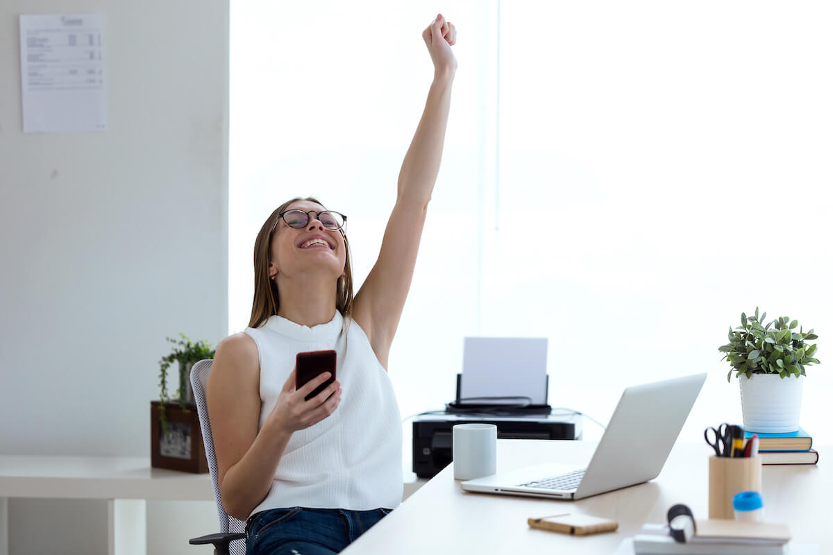 Weekly work plan: entrepreneur holding her phone with her other arm raised, expressing success