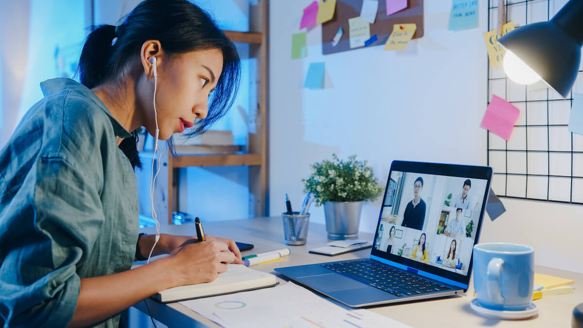 Overwhelmed at work: woman taking down notes while in a virtual meeting