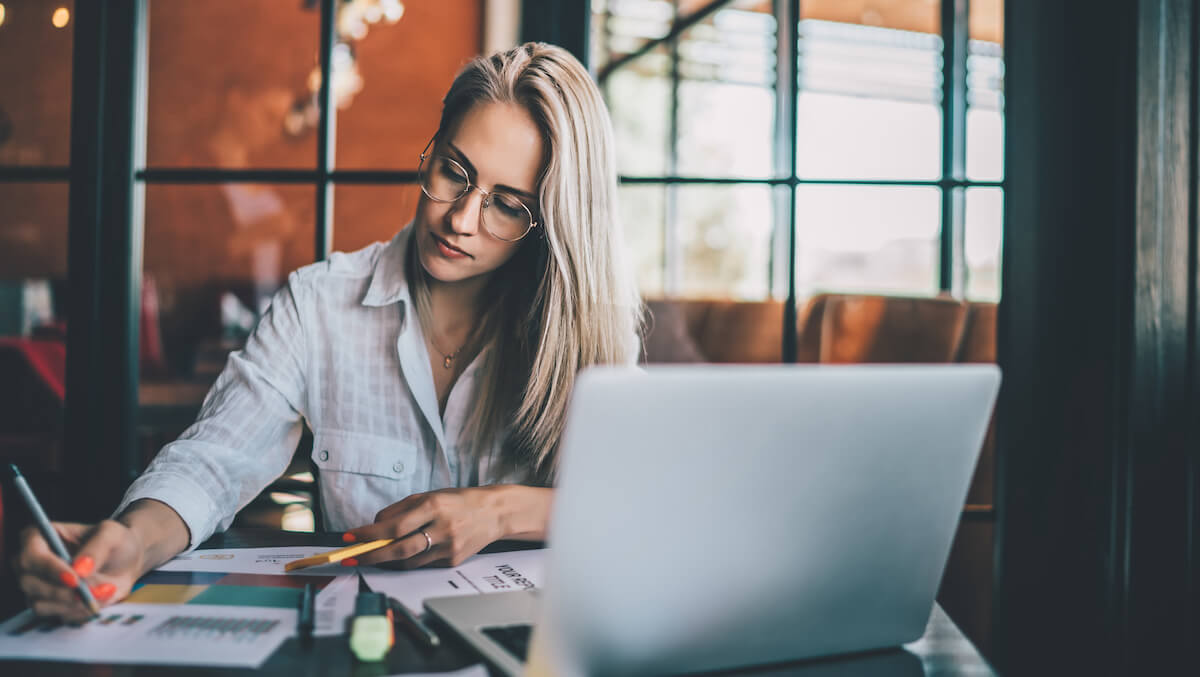 Context switching: A woman sits at a desk with her laptop and writes on a printed chart