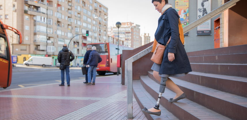 A woman with a leg prosthesis goes to a bus stop.