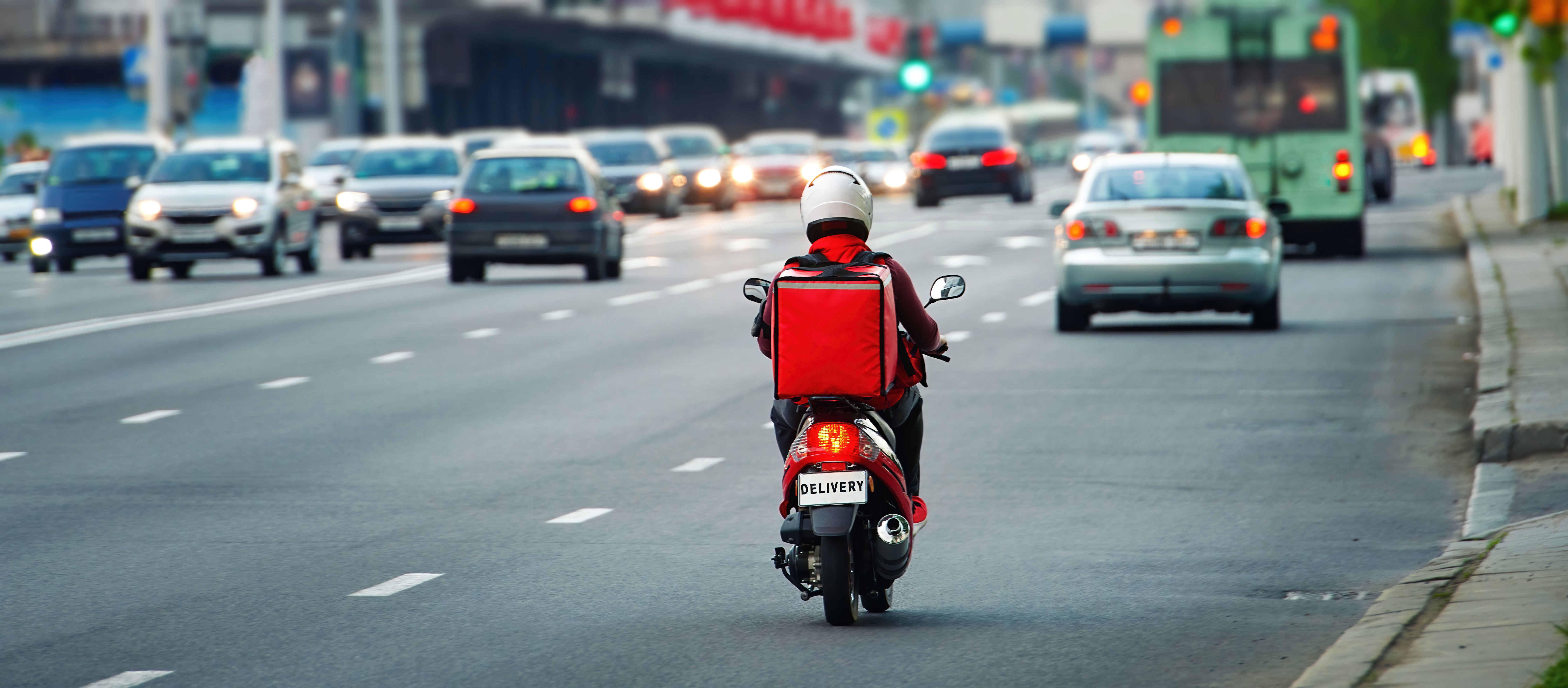 Foto de um motoboy dirigindo pela cidade com uma mochila de delivery nas costas