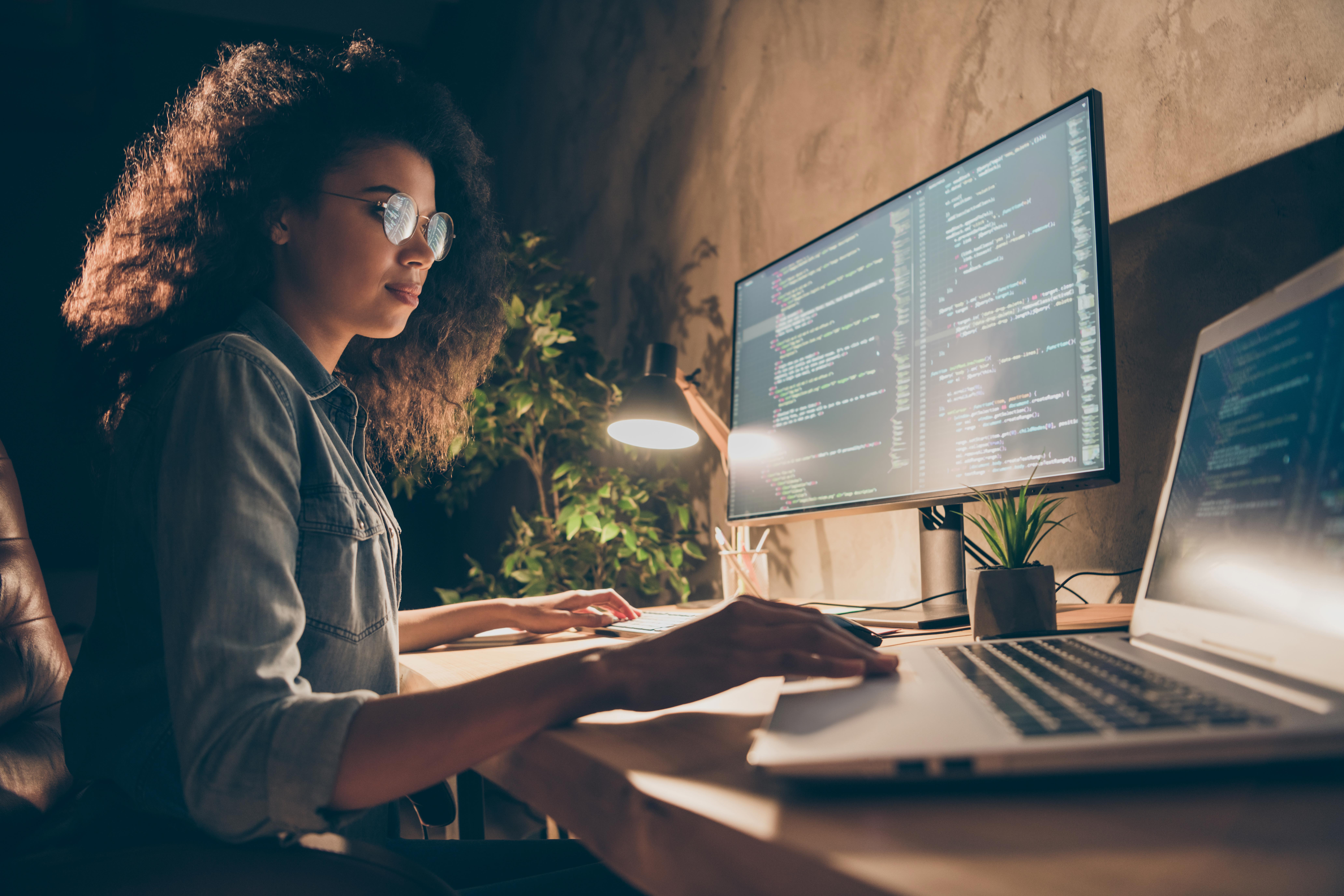 Foto de uma mulher programando com dois computadores
