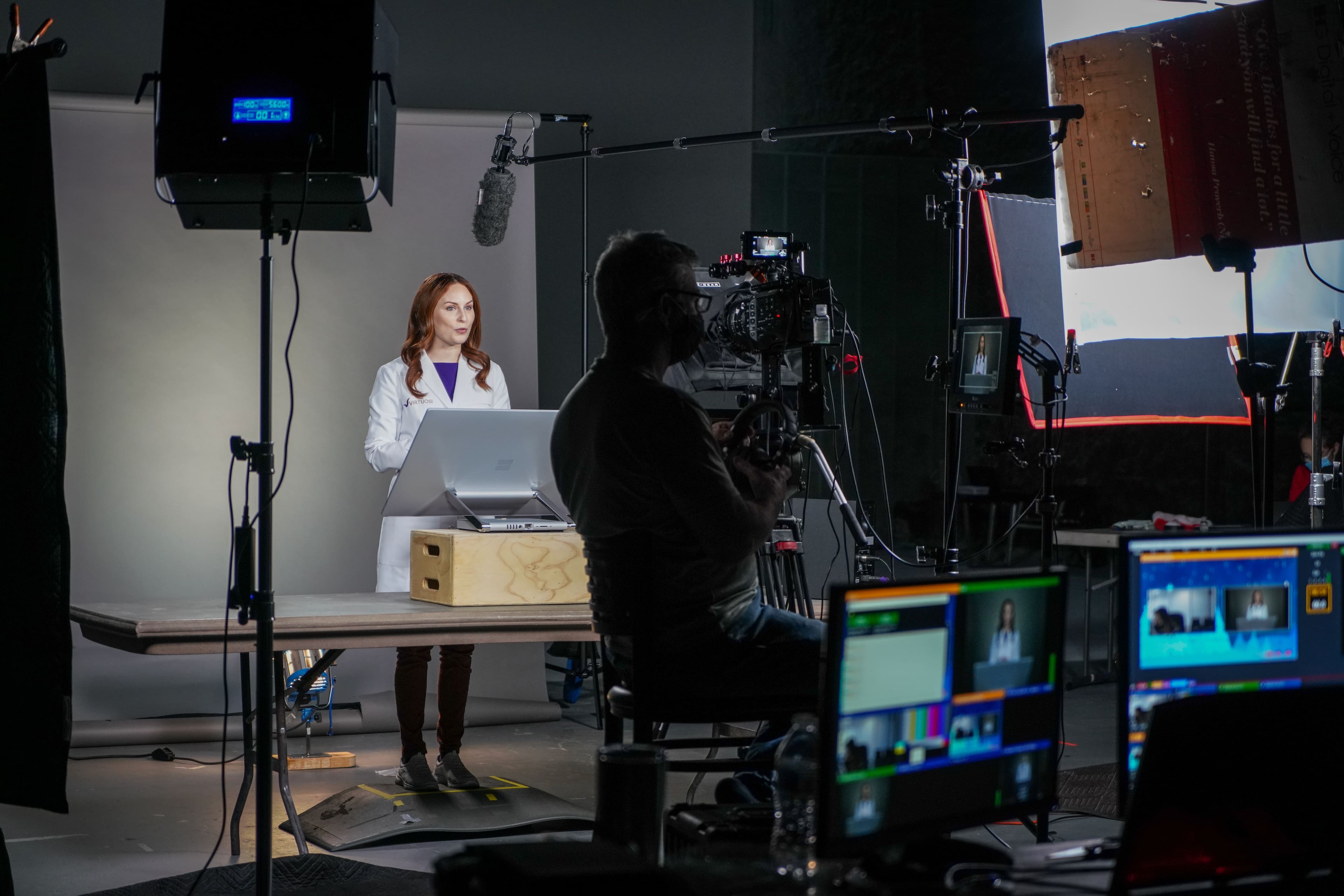 The Development team records a woman giving a talk. In the foreground is all the equipment - video, audio, lighting, etc. - managed bu the development team.