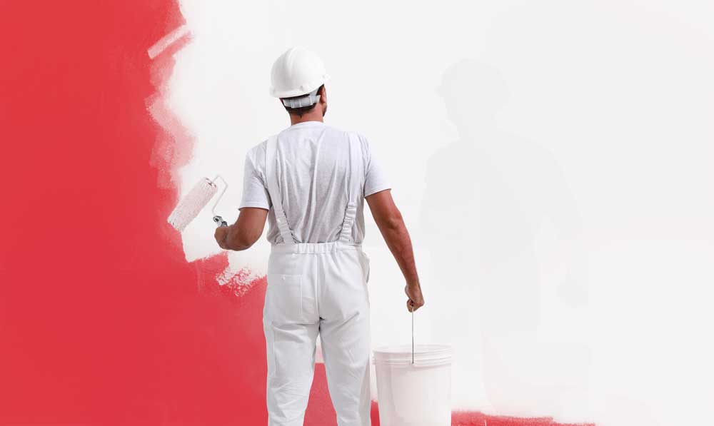 Painter with paint roller painting a wall red.
