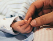 A parent holds their baby's hand