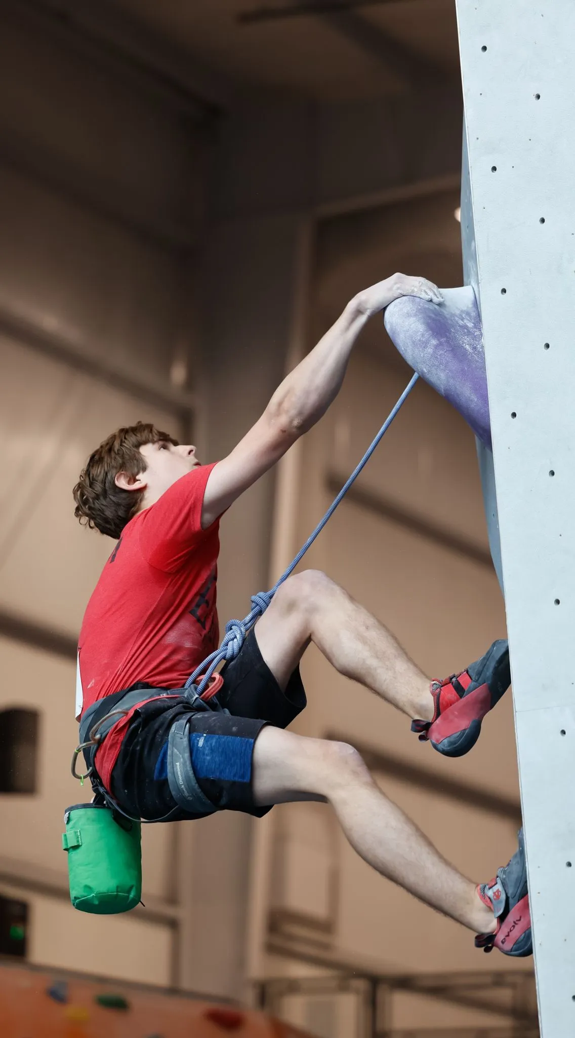 A male rock climber on the wall of an indoor climbing facility.