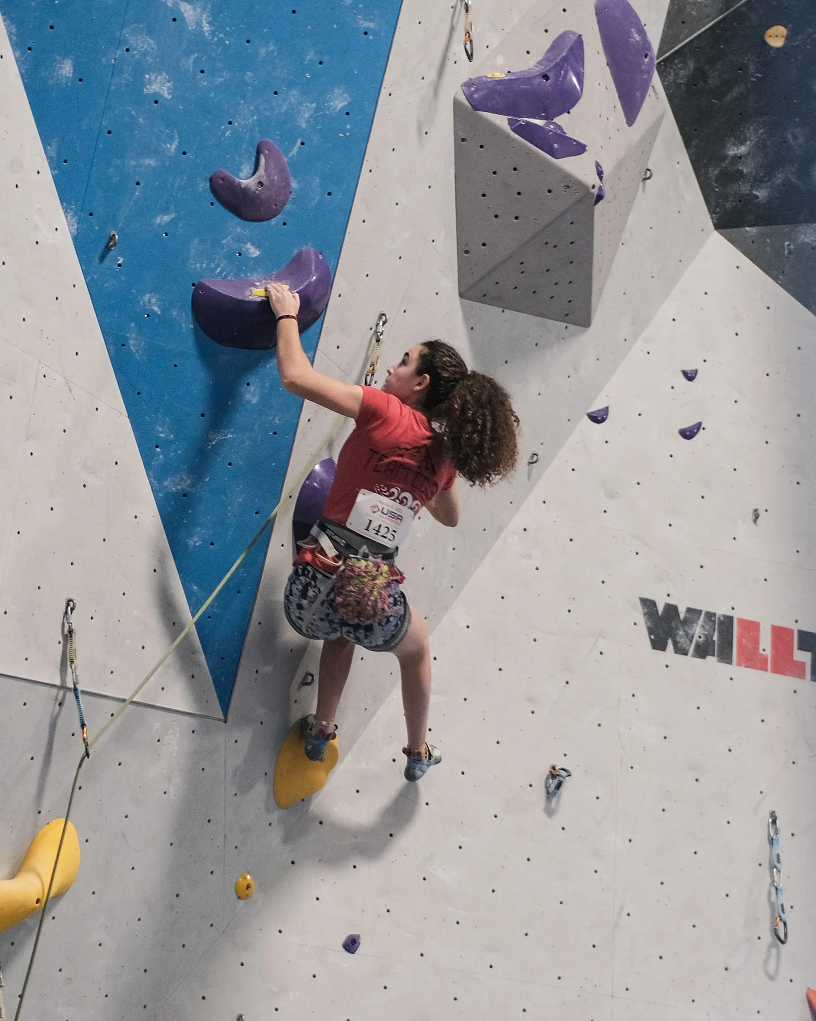 A female rock climber on the wall of an indoor climbing gym.
