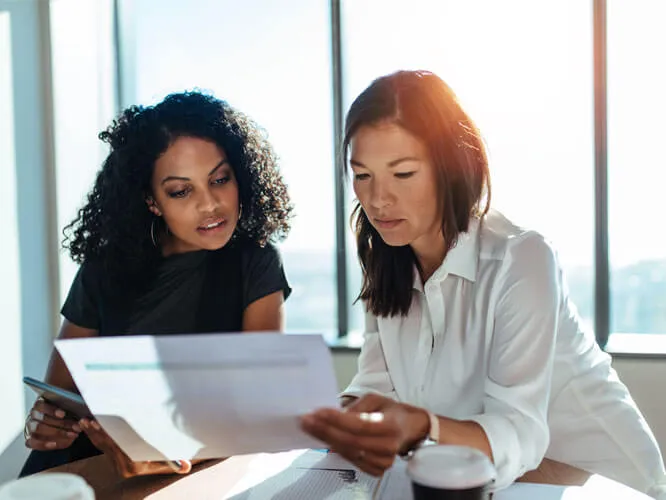 Two females sitting in a boardroom looking at a spreadsheet