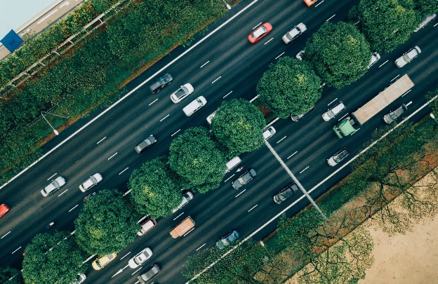 An overhead photo of a busy highway with a row of trees down the median strip