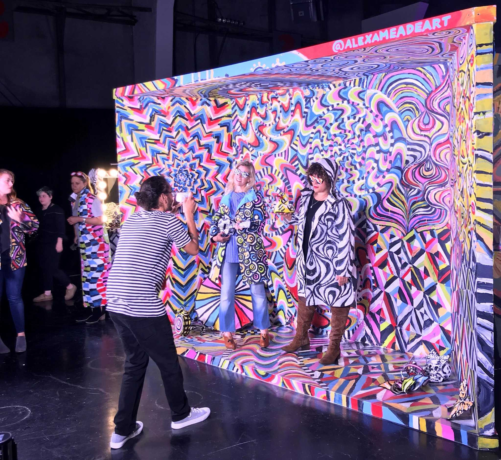 A man takes a picture of 2 women standing next to a colorful background