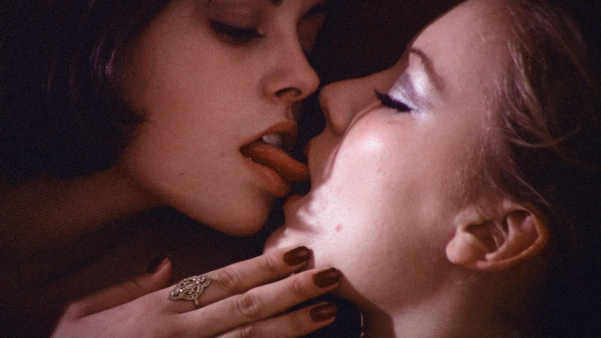 Film still from Doriana Gray. Two women kiss with their eyes closed, one with their tongue pointing out at the other.