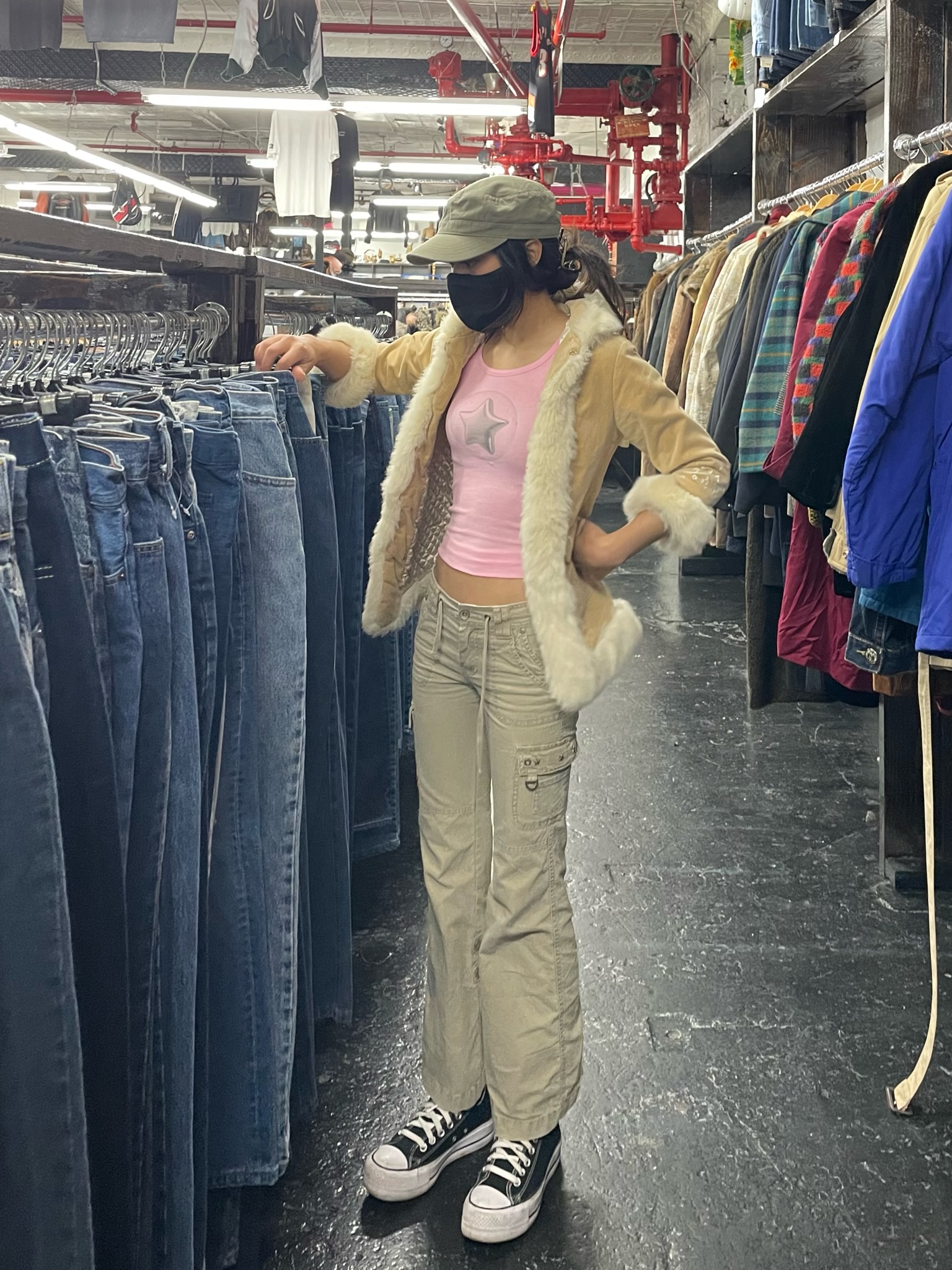 Sammy wearing the bubblegum pink 'Popstar tank' and standing next to a clothing rack using one hand to sort through denim jeans at a thrift store