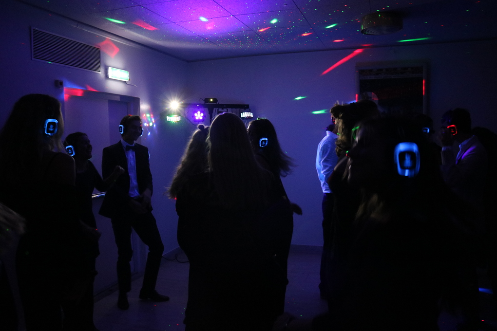 En grupp studenter som dansar i ett nedsläckt rum med discolampor. Studenterna har på sig färgglada hörlurar eftersom att de är på silent disco