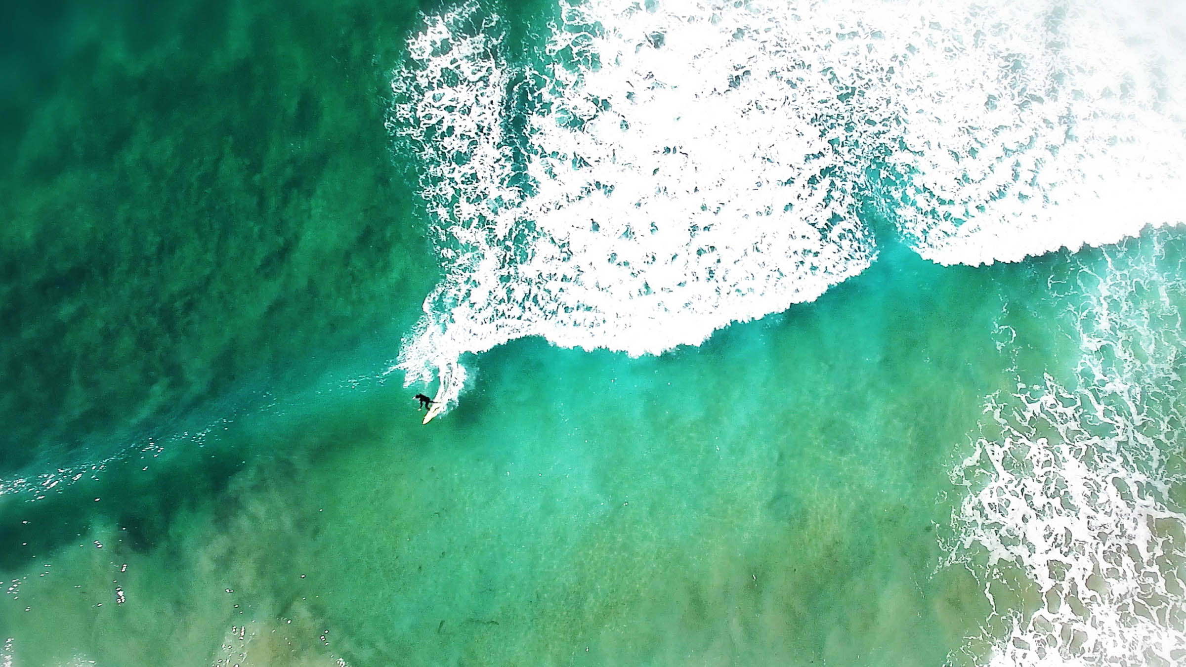 an overhead view of a surfer riding breaking waves
