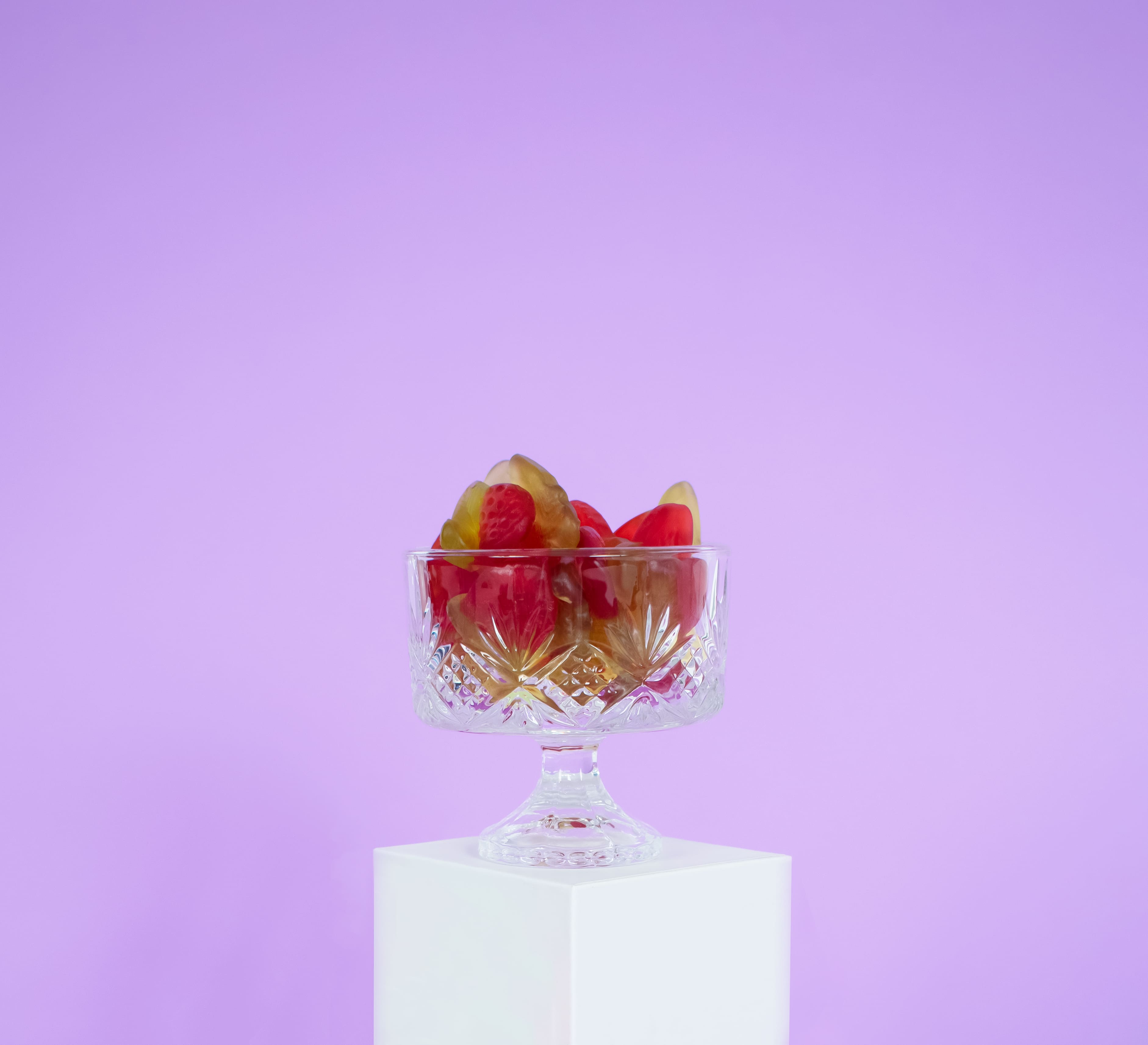 A cup of strawberry gummies in a crystal cup, with a purple background.