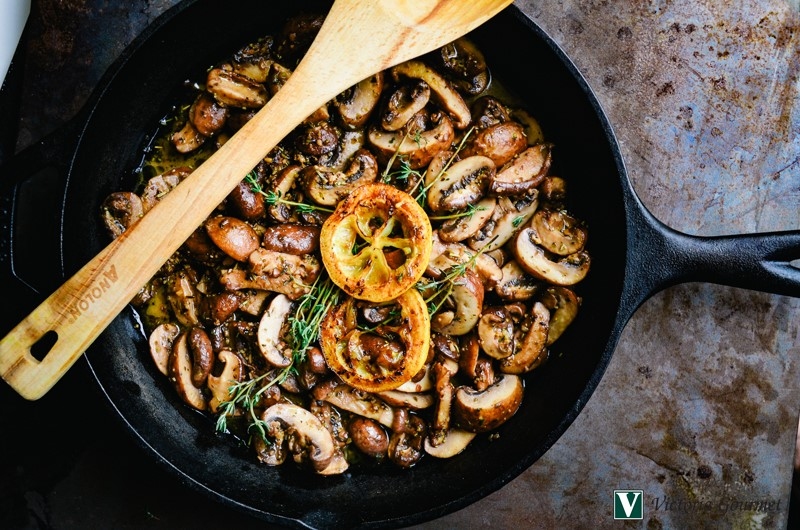 Cast iron skillet with sautéed mushrooms, caramelized lemon and a wooden spoon.