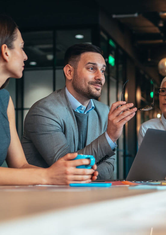 A man is smiling, and confidently leads a team meeting around a table.