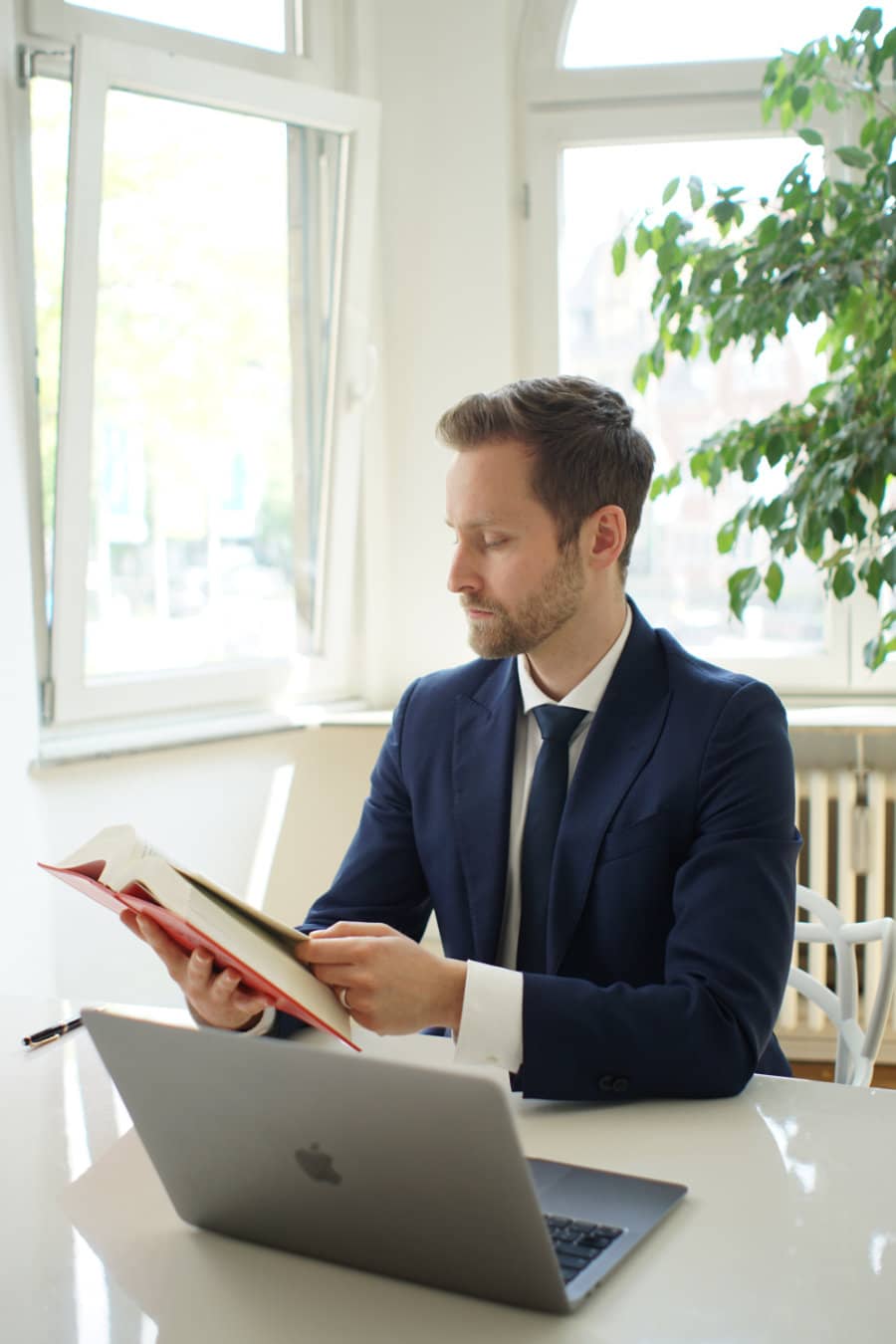 Rechtsanwalt Yazdan Yilmaz mit Buch von Deutschen Gesetzen vor seinem Laptop am Schreibtisch im Profil.