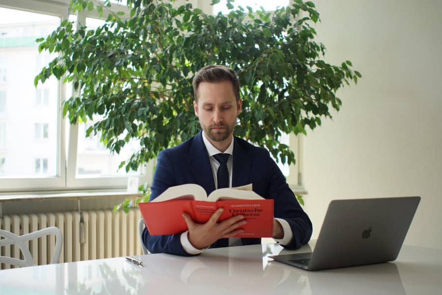 Rechtsanwalt Yazdan Yilmaz mit Buch von Deutschen Gesetzen vor seinem Laptop am Schreibtisch.