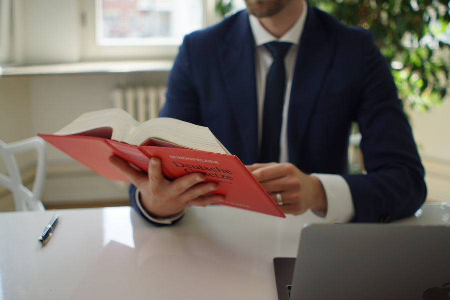 Rechtsanwalt Yazdan Yilmaz mit Buch von Deutschen Gesetzen vor seinem Laptop am Schreibtisch.
