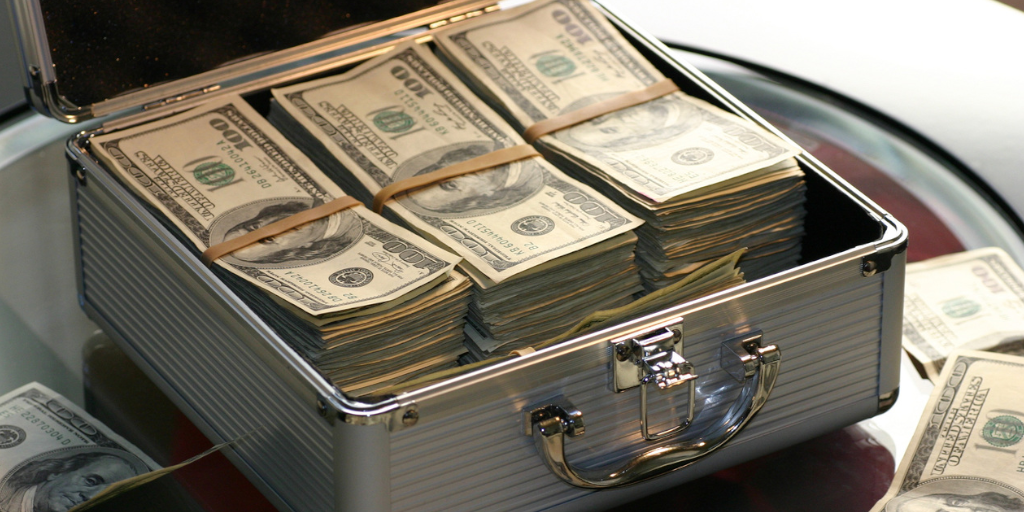 A stack of 100 dllar bills inside an open metal secure case, which is resting on a glass table.