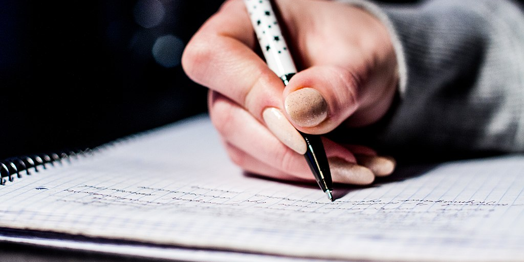 A close-up photo of someone's hand as they hold a pen and take notes