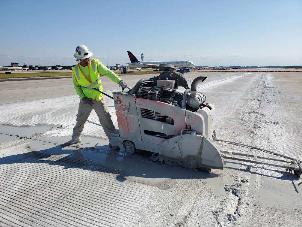 A Diamond Drilling and Sawing crew member sawing concrete slab on a ATL airport runway