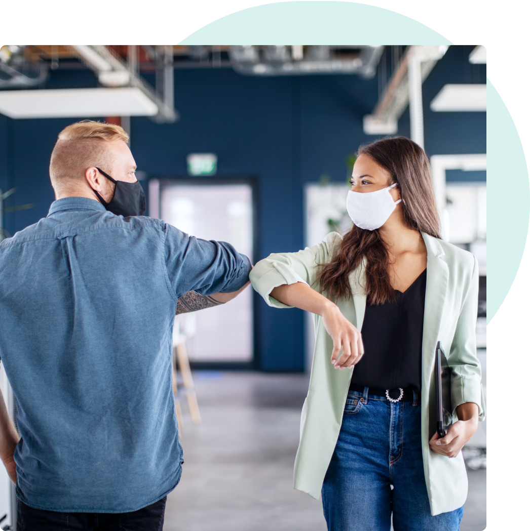 Two young, professional employees with protective masks shoulder bumping each other