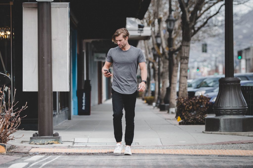 A younger male walking down the sidewalk while looking at his phone.