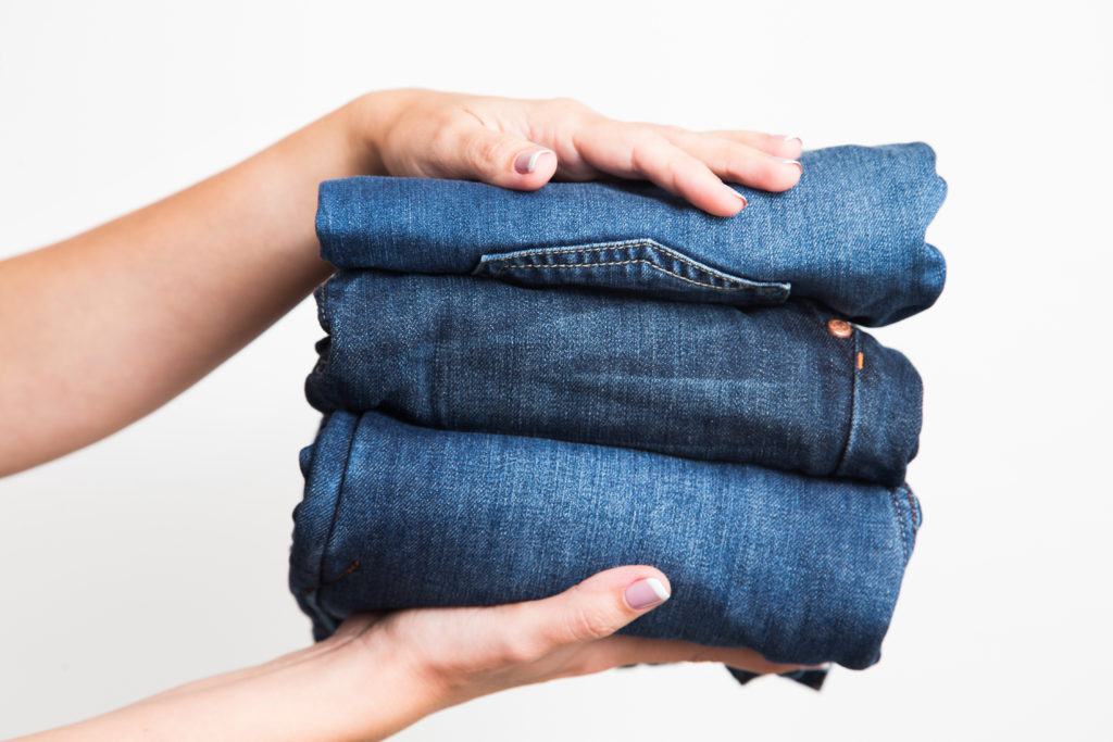 Hands holding three pairs of jeans, their production contributing to fashion's water footprint