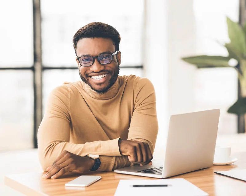 A smiling man sitting next to a laptop