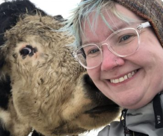 A woman with glasses and a blue fringe shares the frame with a cow