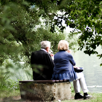 Older retired couple sitting outdoors on a bench enjoying the scenery 