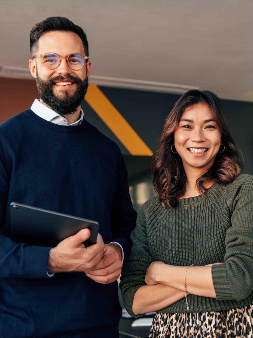 Man holding a laptop standing next to a woman. Both smiling.